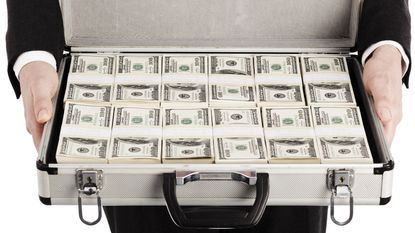 A man in a suit holds a briefcase of money.