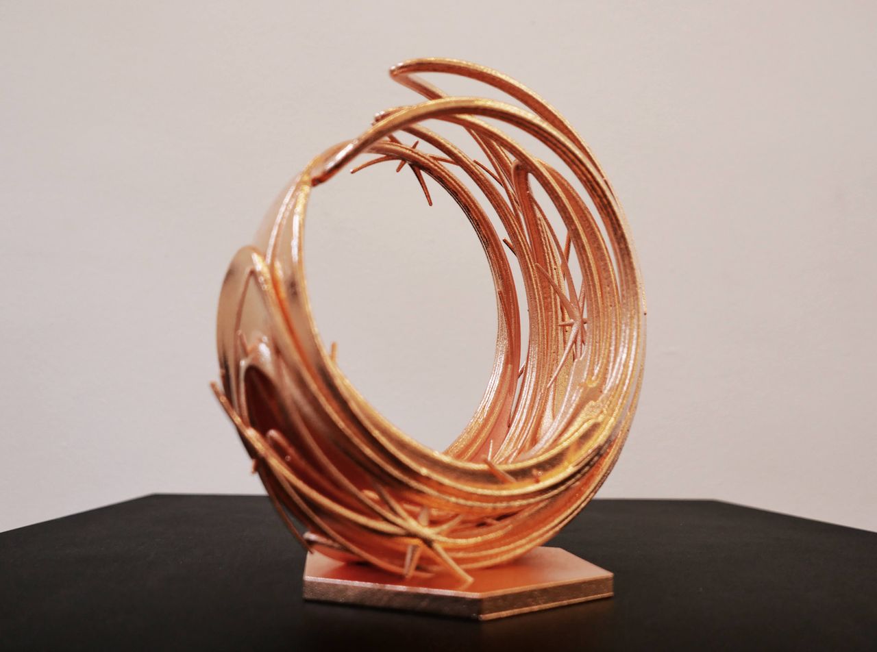 A circular golden metal sculpture sits on a dark surface.