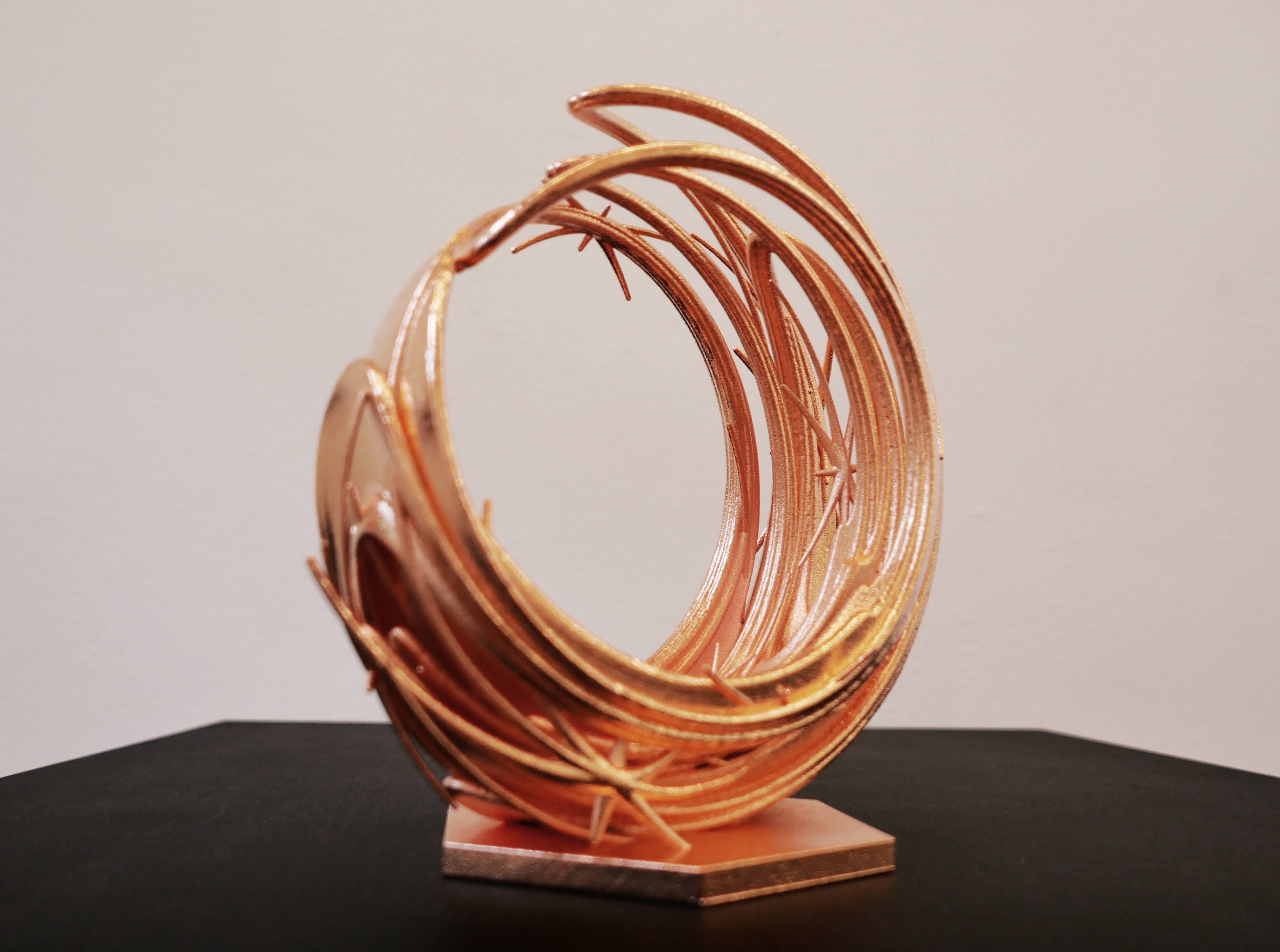 A circular golden metal sculpture sits on a dark surface. 
