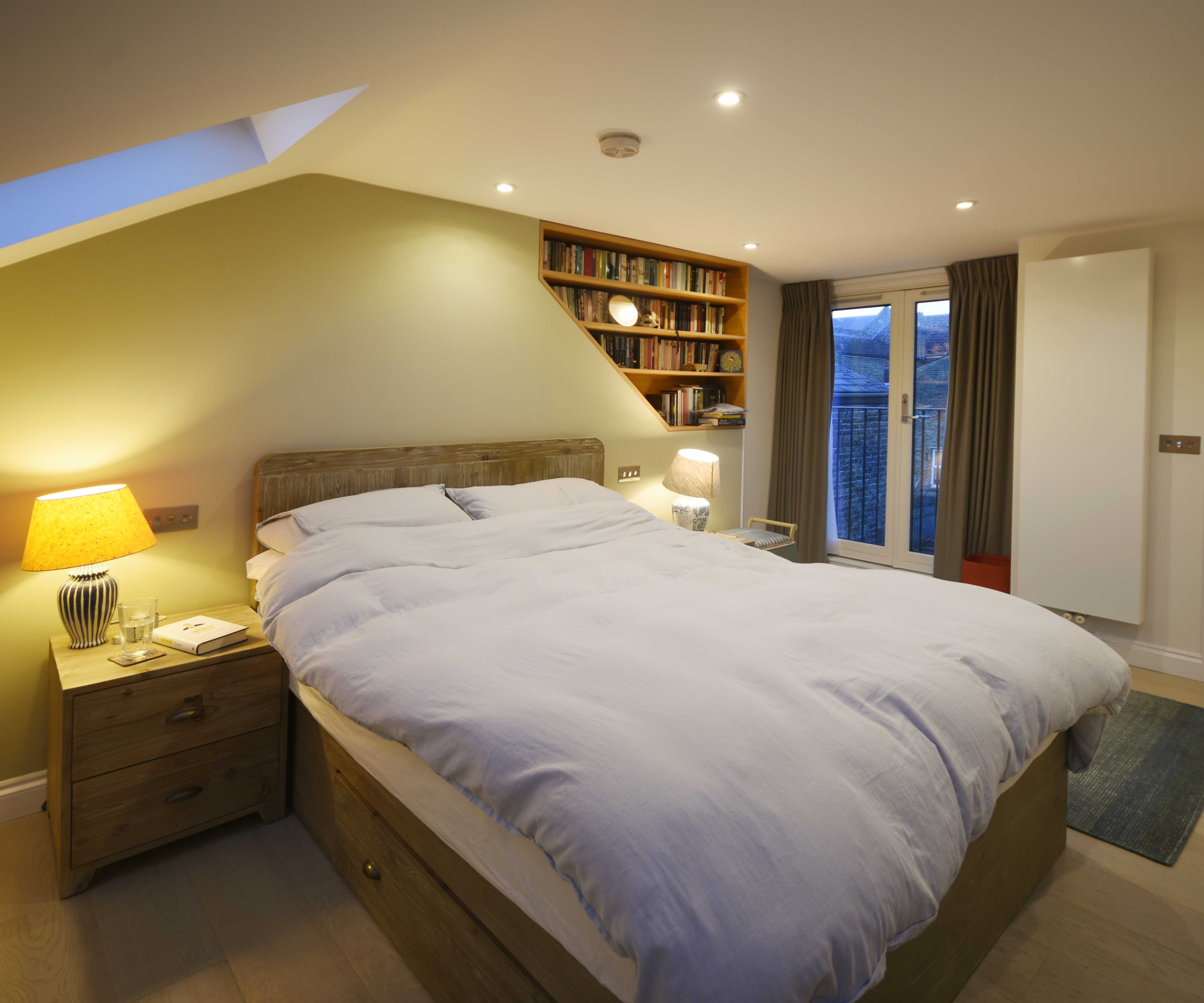 bedroom in loft conversion with book shelving built into one side of the wall behind the bed