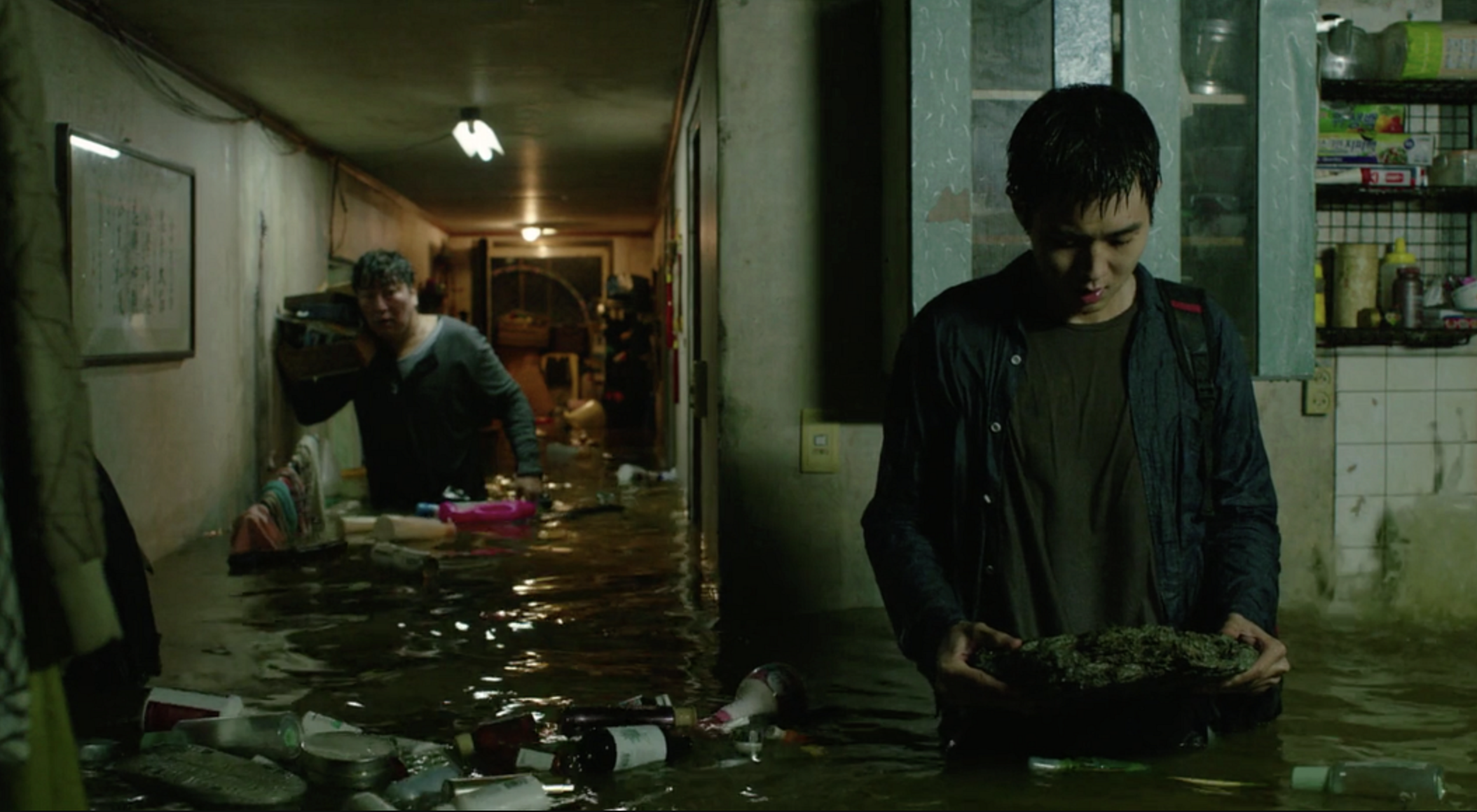 Two men stand in a flooded apartment and look at their destroyed belongings.