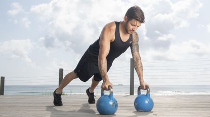 Luke Zocchi performs push-ups while holding onto kettlebells 