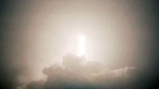 the bright white thrust from a launching rocket is seen through the fog surrounding the launch pad