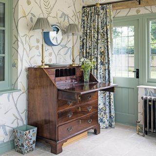 antique bureau in hallway with green and white botanical wallpaper and antique lights
