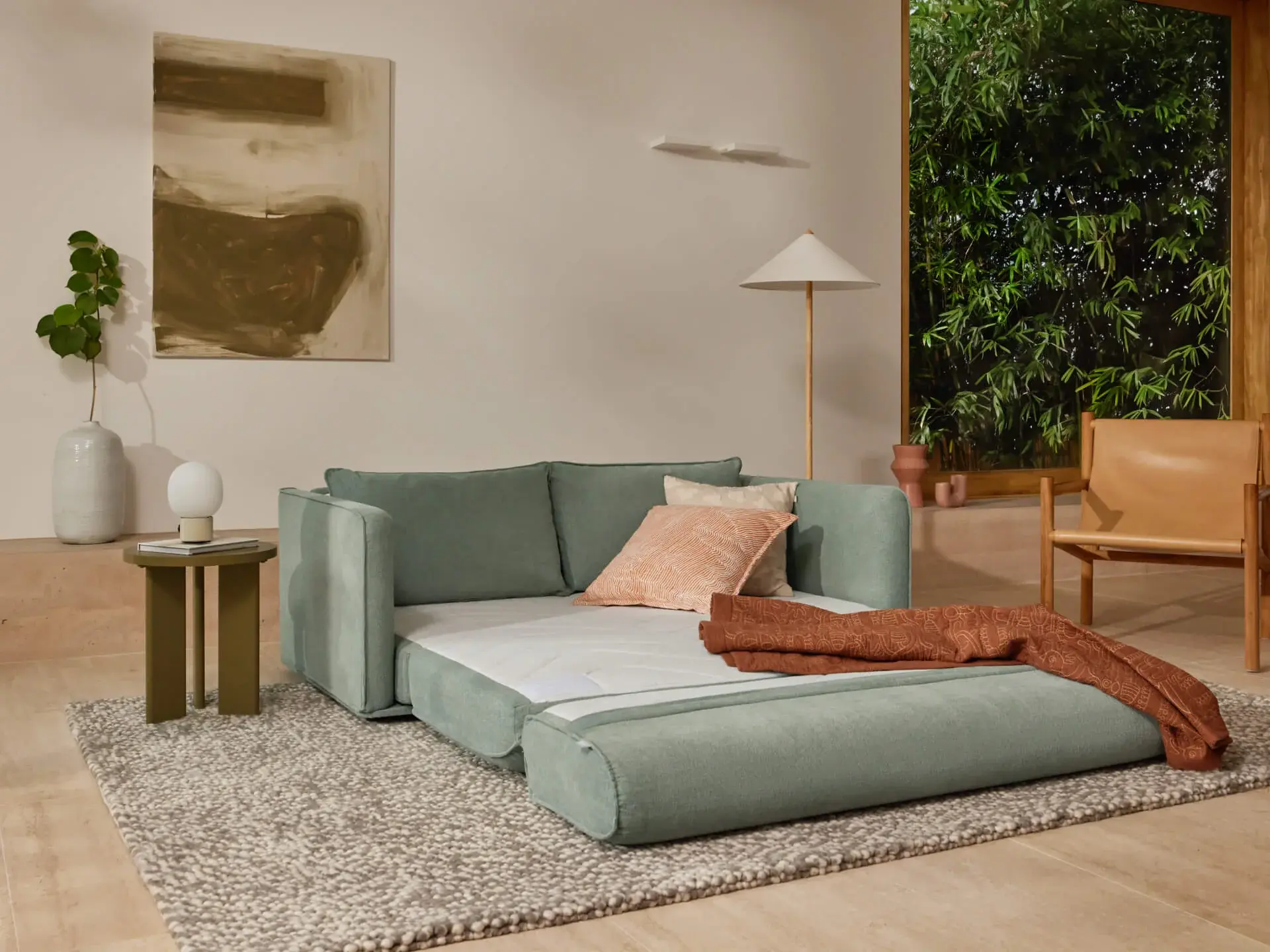 A queen sized Koala sofa bed in gumleaf green, with two cushions and a throw on top.
