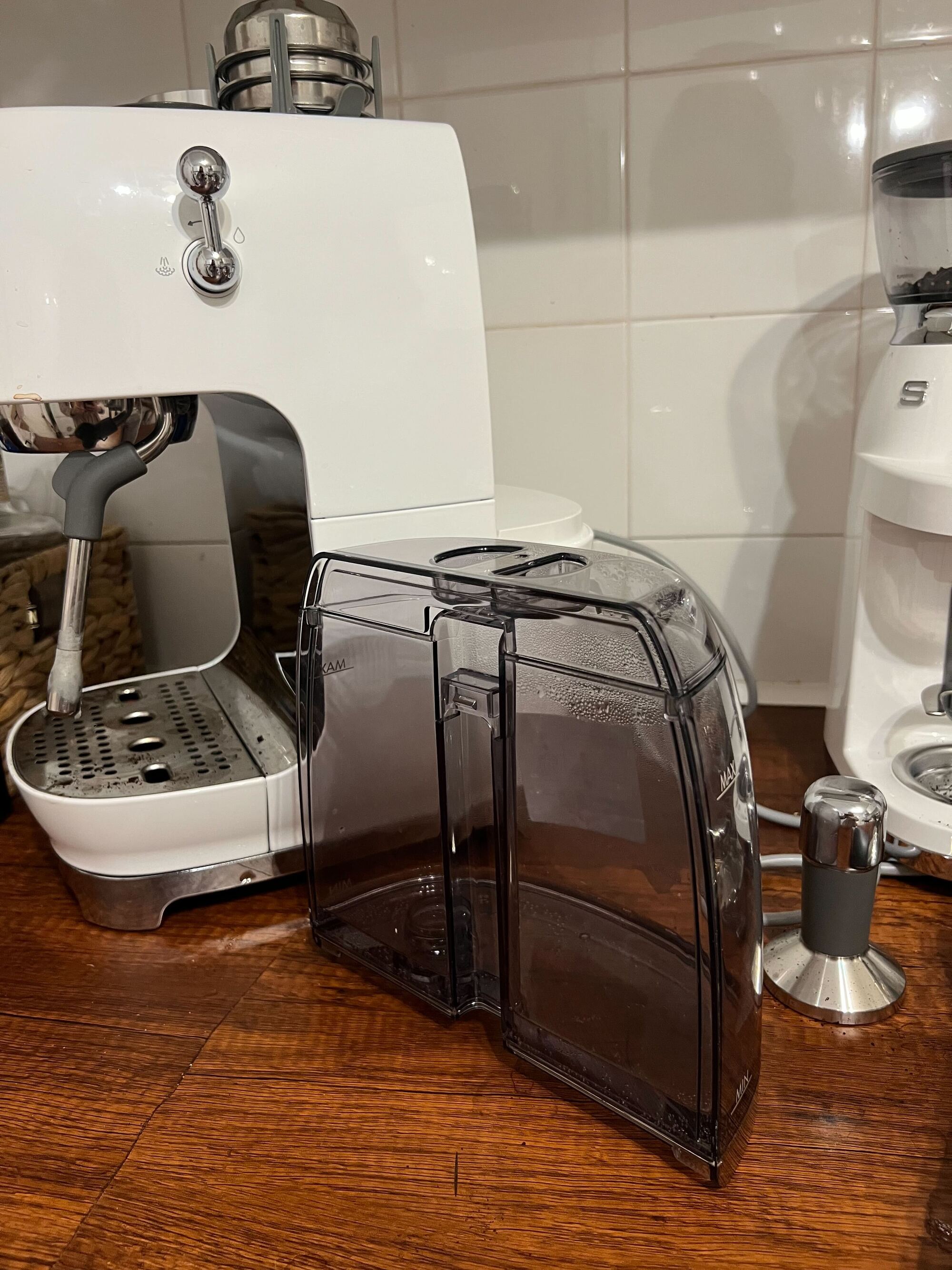Image of the gray water tank removed from the white Smeg cold brew machine sitting on the countertop in front of the machine.