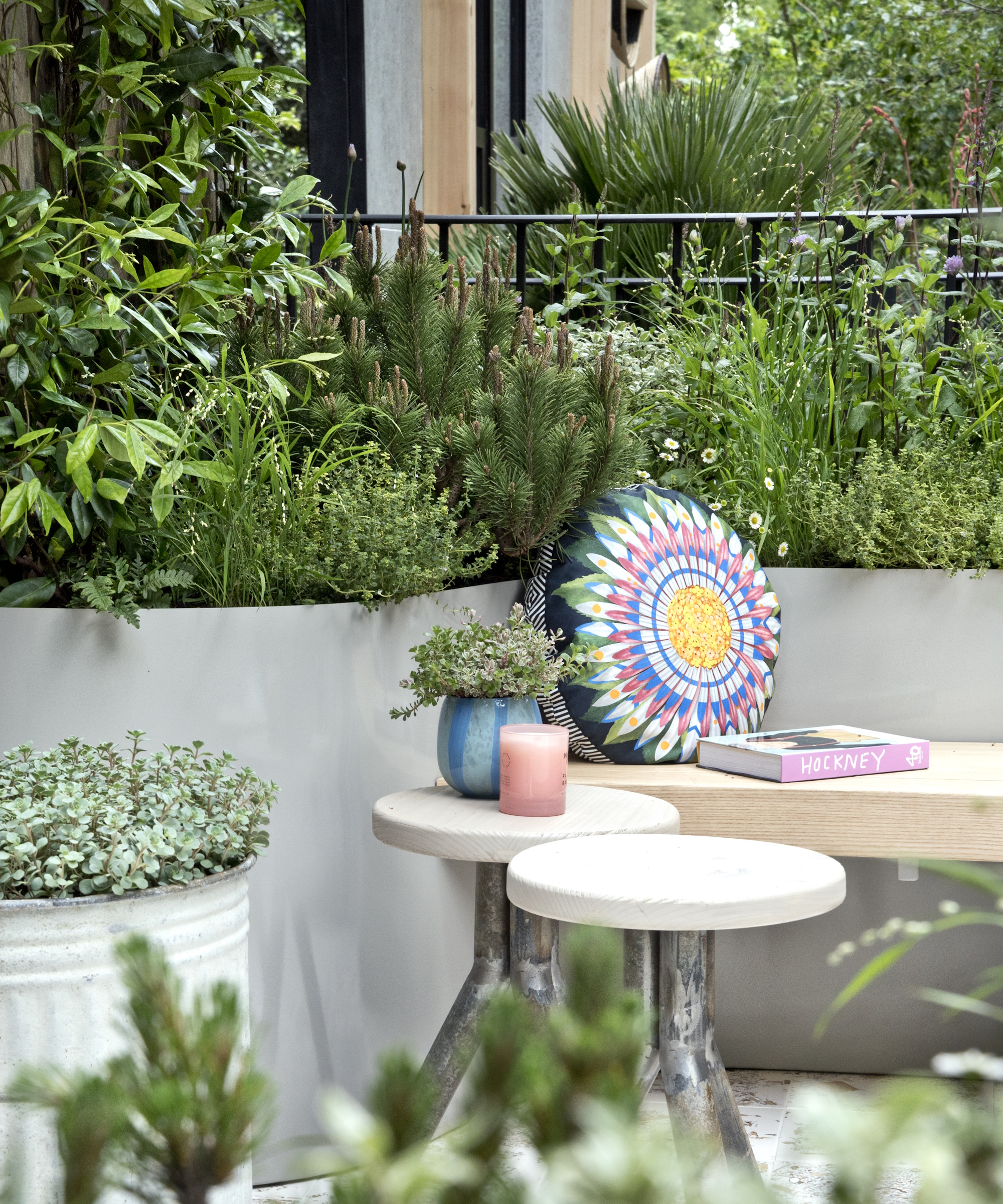 Small seating area in a garden with colourful round cushion, green planting and round stools