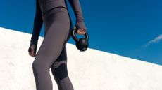 Woman holding small kettlebell wearing workout clothes to do standing ab exercises in the sunshine against blue sky