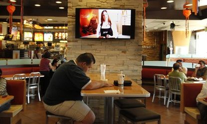 A customer sits at a table near an HDTV screen playing McDonald's new TV channel, which is being tested in California before a national rollout.