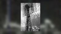 a black and white image of a radio antenna set against the clouds in the sky