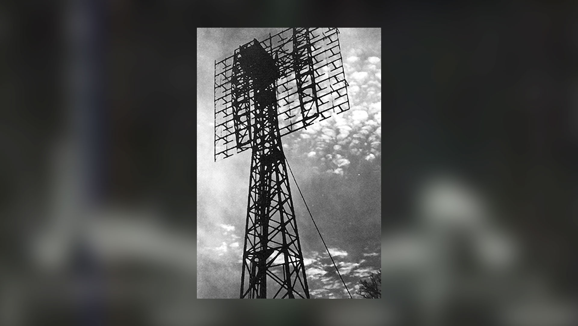 a black and white image of a radio antenna set against the clouds in the sky