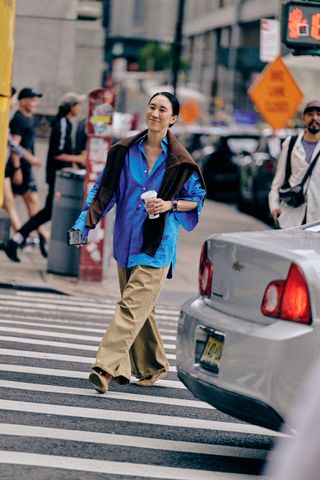 Eva Chen at New York Fashion Week in a blue button-down, brown sweater, and tan pants