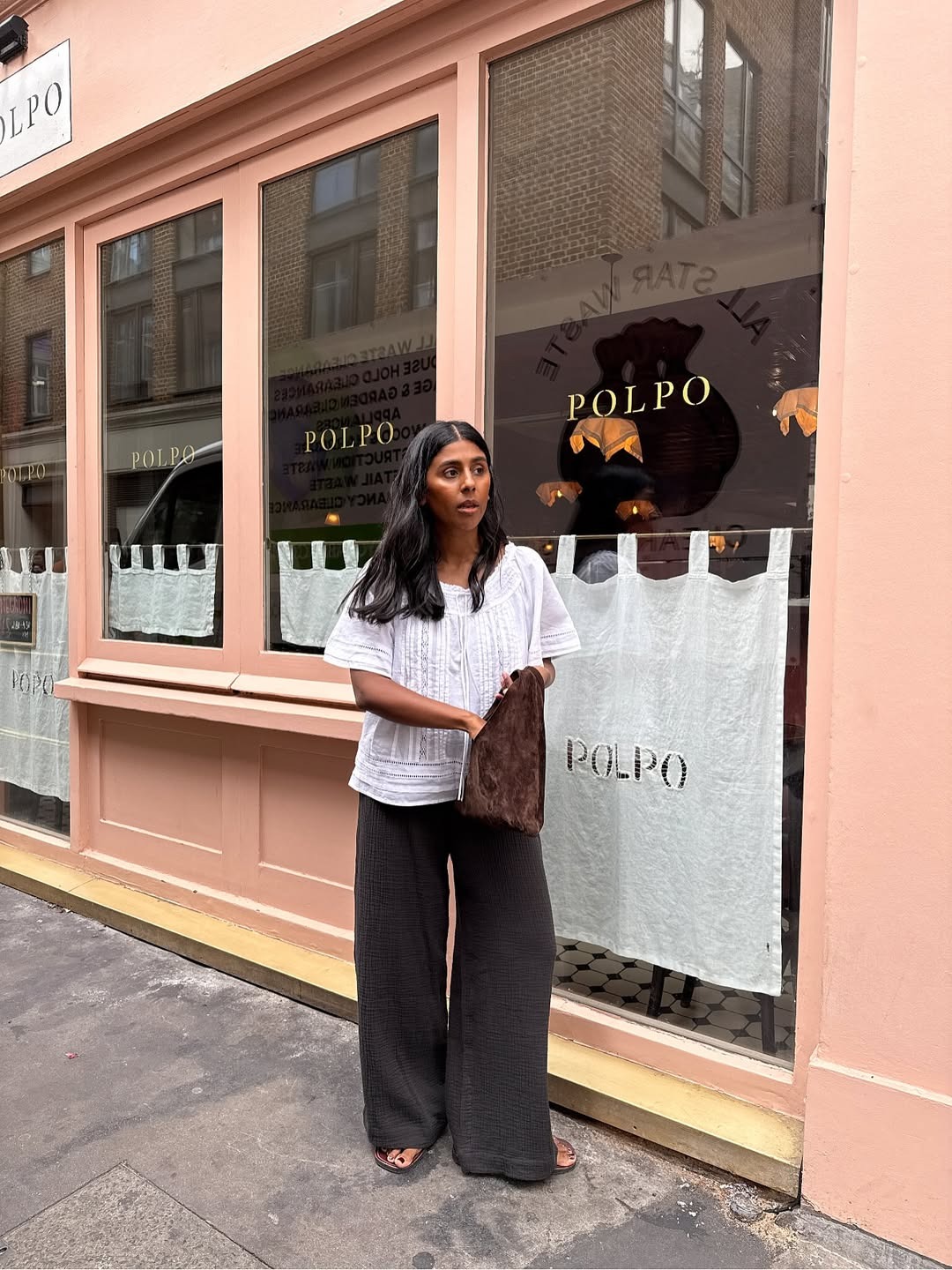 Monikh wears pretty white blouse with brown wide leg trousers and flip flops while carrying a suede bag.