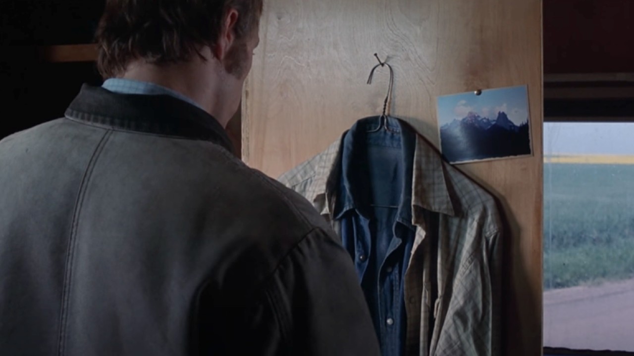 Ennis looking at the jacket and picture of a mountain.