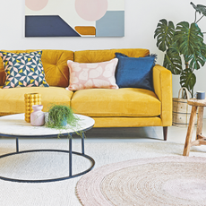 Textured crcular rug placed on white rug. Round coffee table and yellow sofa with blue cushions