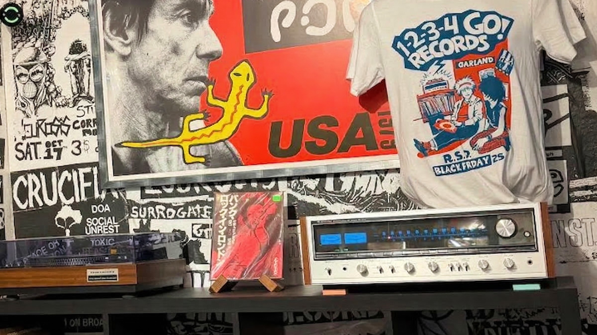 A vintage stero and turntable take pride of place on a bookshelf, flanked by punk posters and memorabilia. The image of Iggy Pop was slightly edited by Gemini.