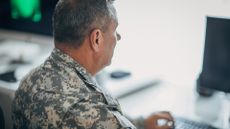 US Army National Guard personnel pictured sitting in uniform while working on a desktop computer.