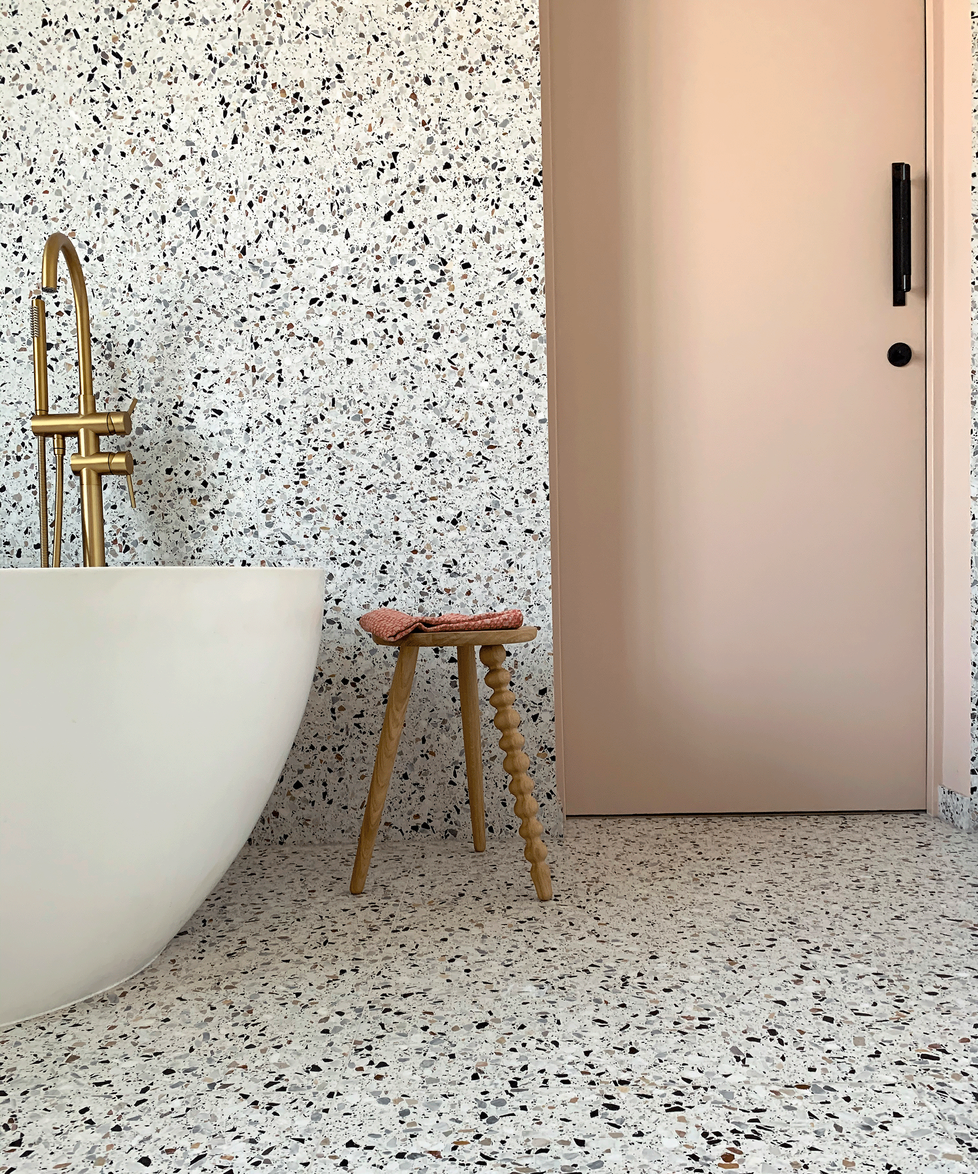 bathroom with matching terrazzo wall and floor with bath and stool