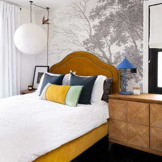 bedroom with grey tree print wall yellow bed with designed cushions and lamp