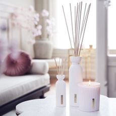 Rituals Sakura reed diffusers, mini and large, next to candle all in white ceramic ribbed vessels in living room on table