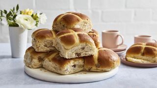 The Best 4 Extra Fruity Hot Cross Buns on a board with flowers and a coffee cup