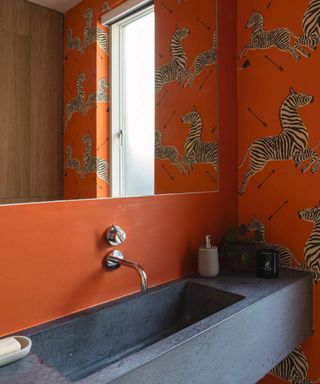 Orange powder room with zebra print wallpaper and dark gray sink
