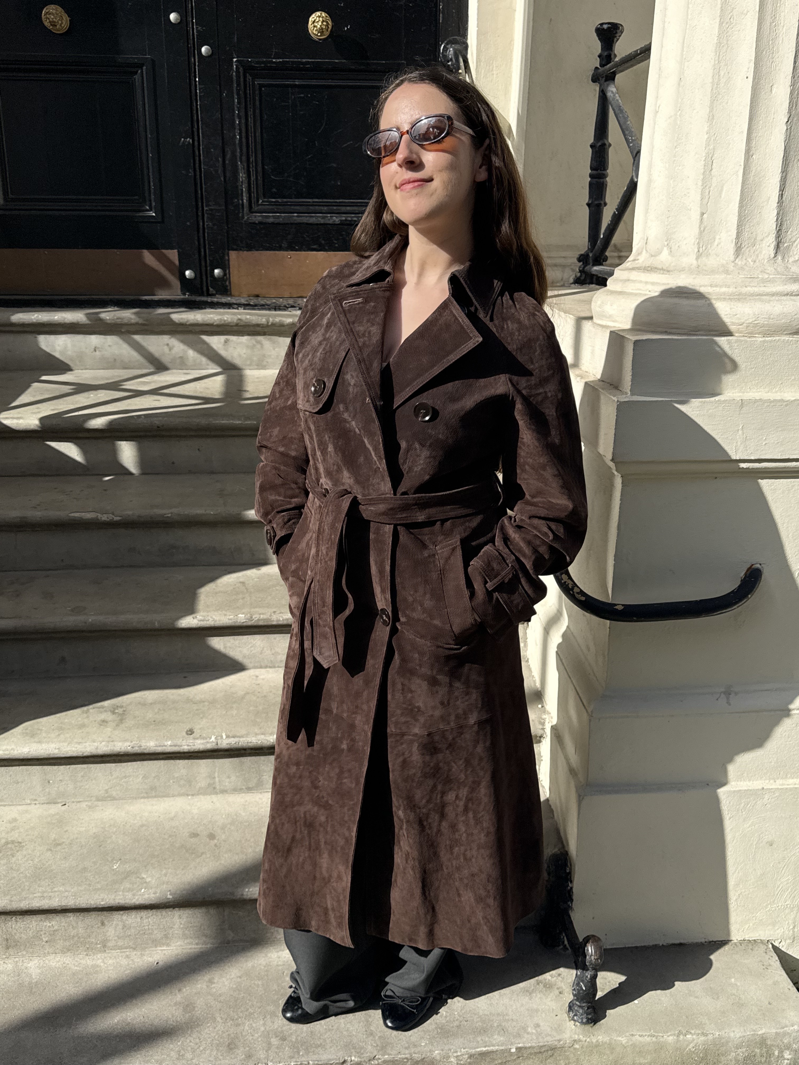 An image of SEO Writer, Ava Gilchrist, wearing a brown suede trench coat with dark grey trousers.
