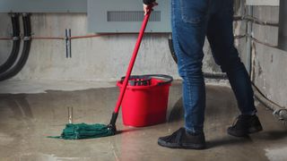 Man in a basement clearing up a water leak with a red mop and bucket
