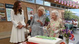 Queen Elizabeth II considers cutting a cake with a sword, lent to her by The Lord-Lieutenant of Cornwall