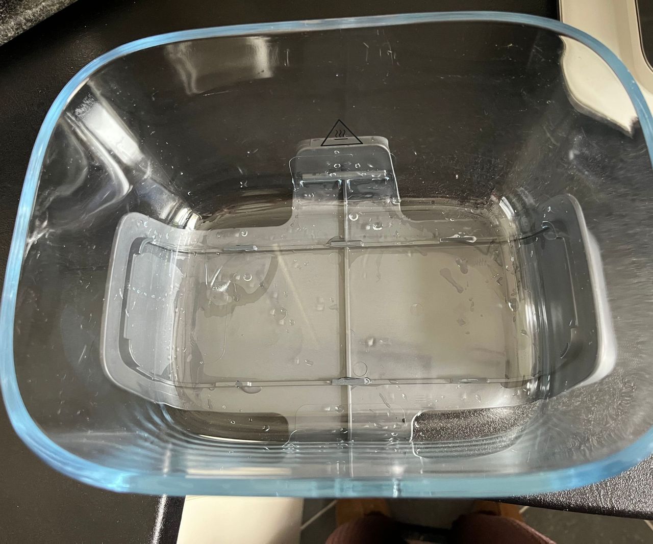 A glass air fryer basket viewed from above with water stuck under it
