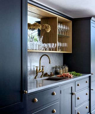 A mirrored background lines an open wooden cabinet in a navy kitchen