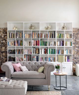 large white bookshelves full of books against a natural stone wall with chesterfield sofa in beige