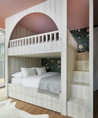 An Ali Budd bunk bed on a wooden floor beneath a pink ceiling.