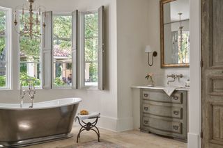 Elegant French-style bathroom with shutters, roll top bath, antique furniture and chandelier