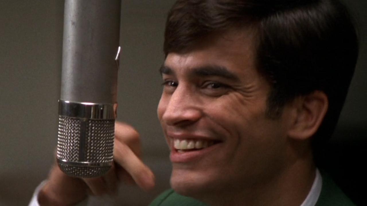 Johnathon Schaech smiles sarcastically while snapping his fingers in That Thing You Do!