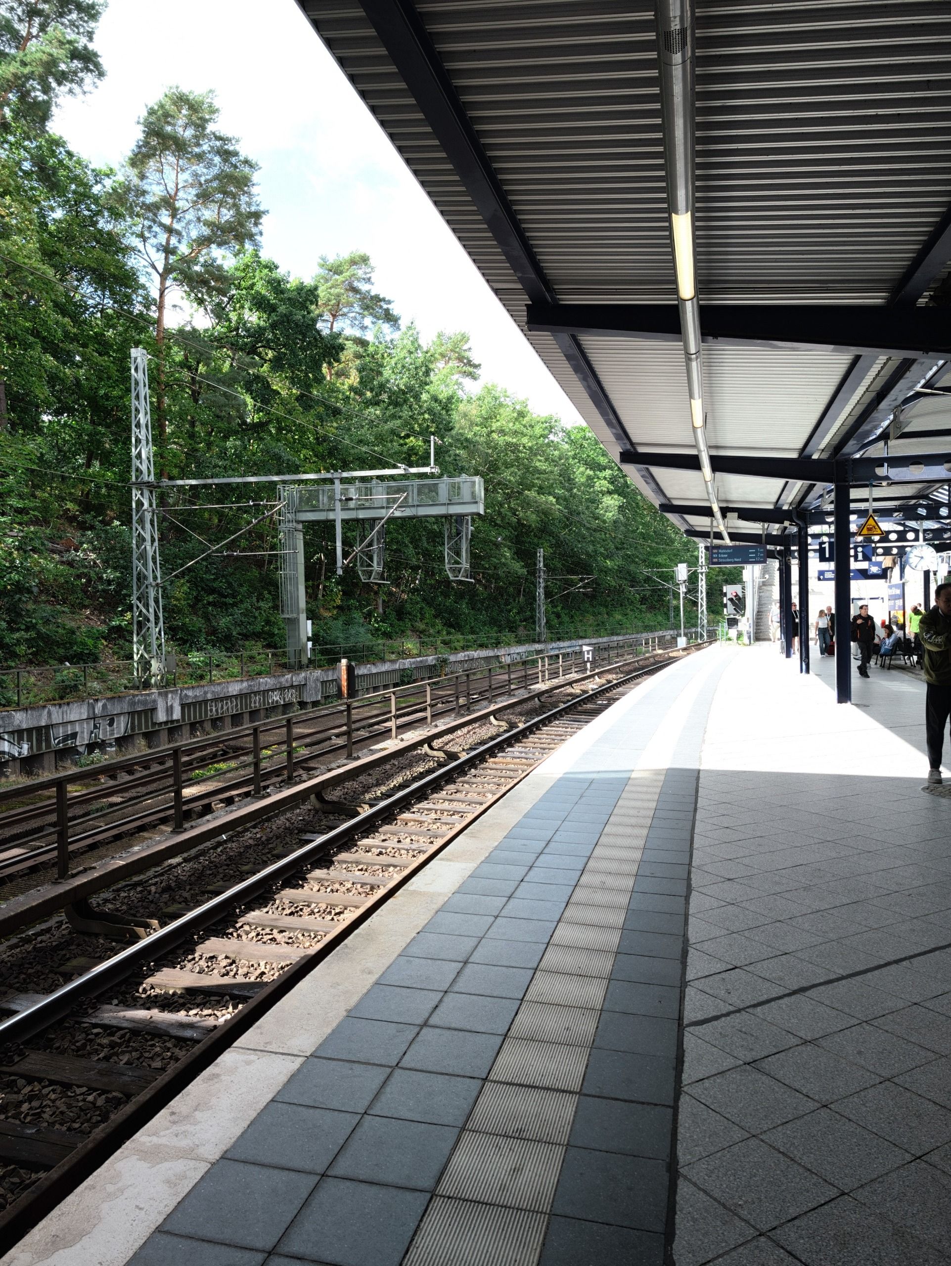 Quiet railway platform with tracks running alongside wooded embankments.
