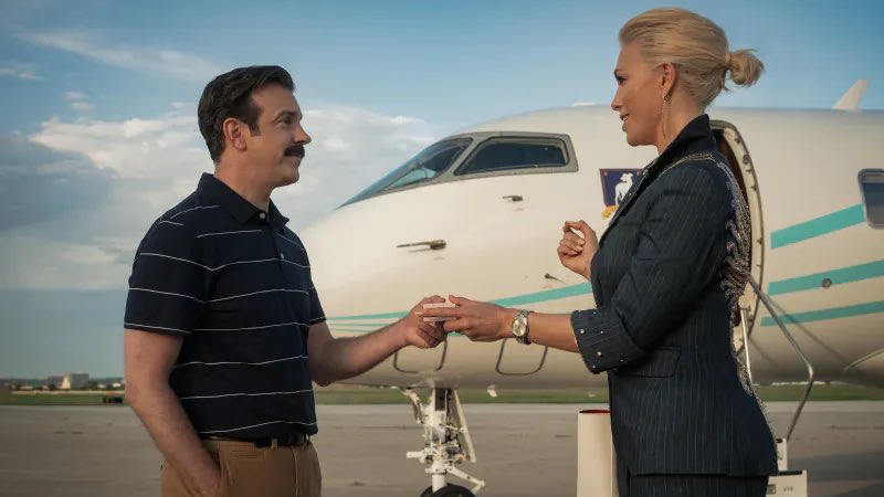 L-R: Ted Lasso (Jason Sudeikis) and Rebecca (Hannah Waddingham) stand in front of an AFC Richmond-branded plane in a first-look still from "Ted Lasso" season 4