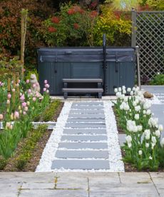 A black hot tub behind a stone path with tulips 