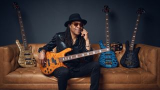 Doug Wimbish sitting on a sofa, holding one of his signature basses, with more of his signature Spector basses placed next to him