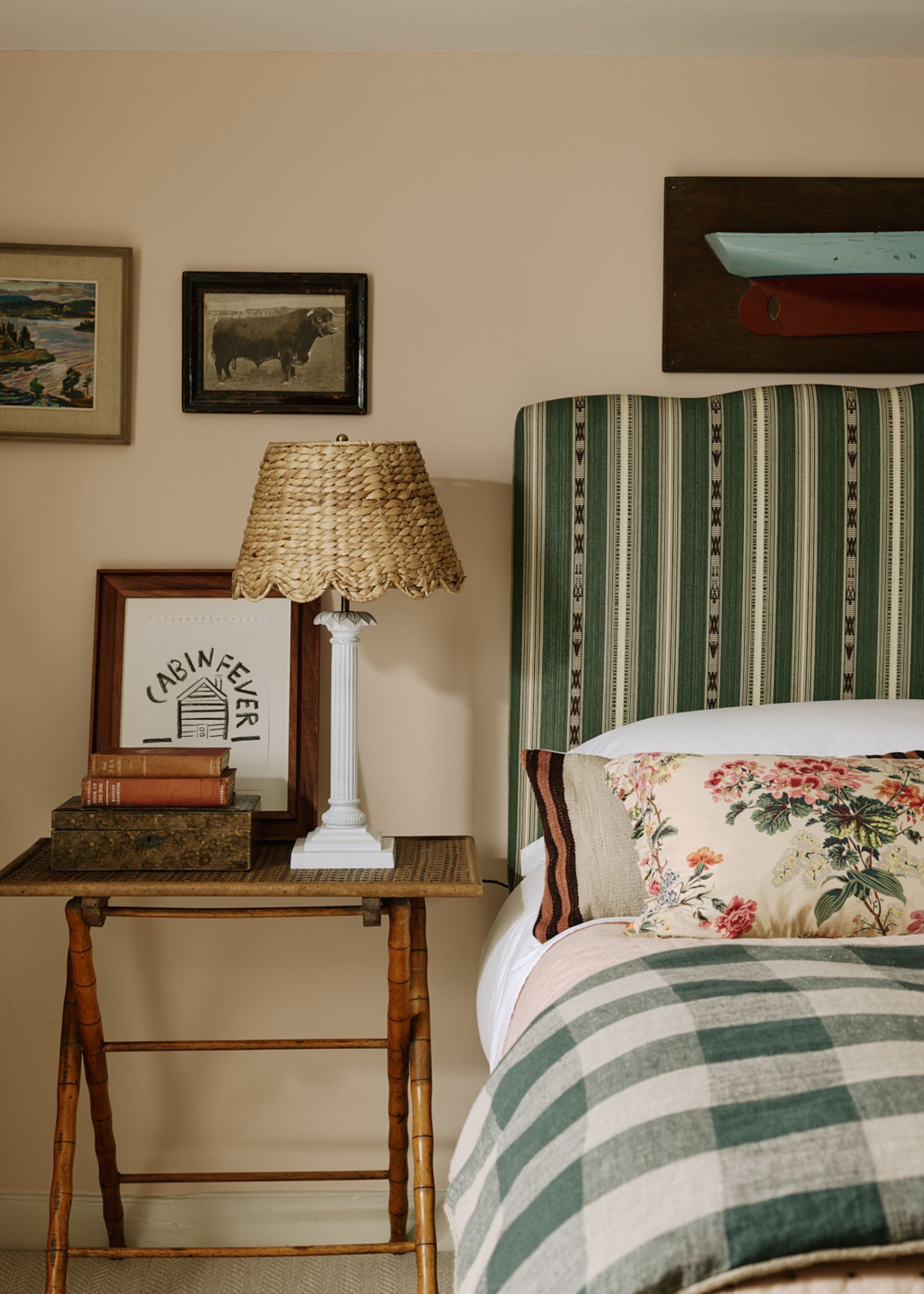 A bedroom with plaster pink walls, a green striped headboard, and a wooden nightstand.