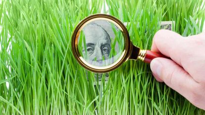 Looking through a magnifying glass at a $100 dollar bill hiding in grass