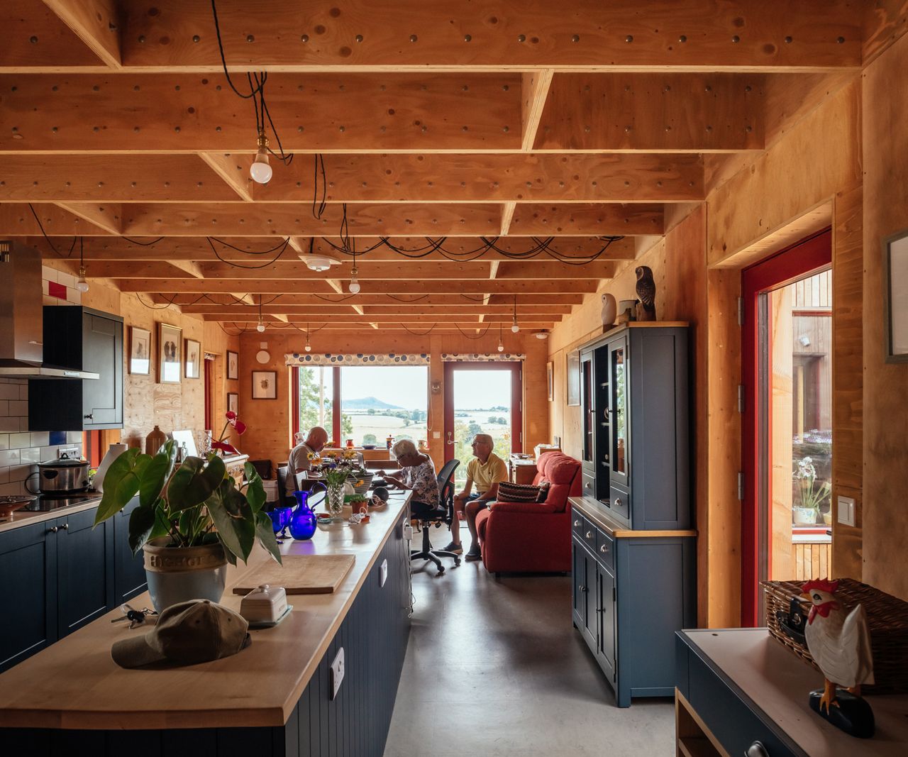 Open plan kitchen and living room space built using a modular build system with timber panels. The homeowners sit in the background living room area