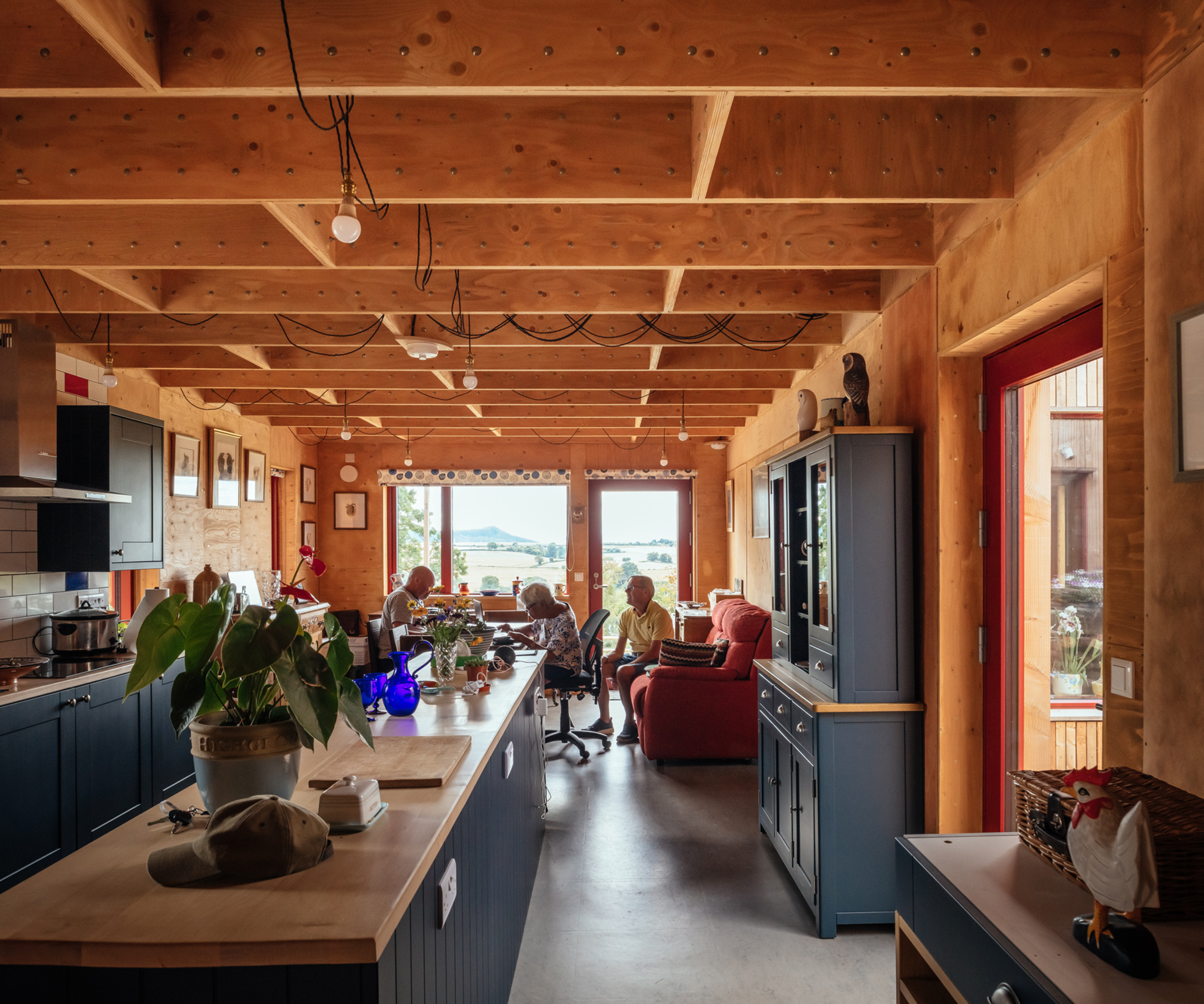 Open plan kitchen and living room space built using a modular build system with timber panels. The homeowners sit in the background living room area