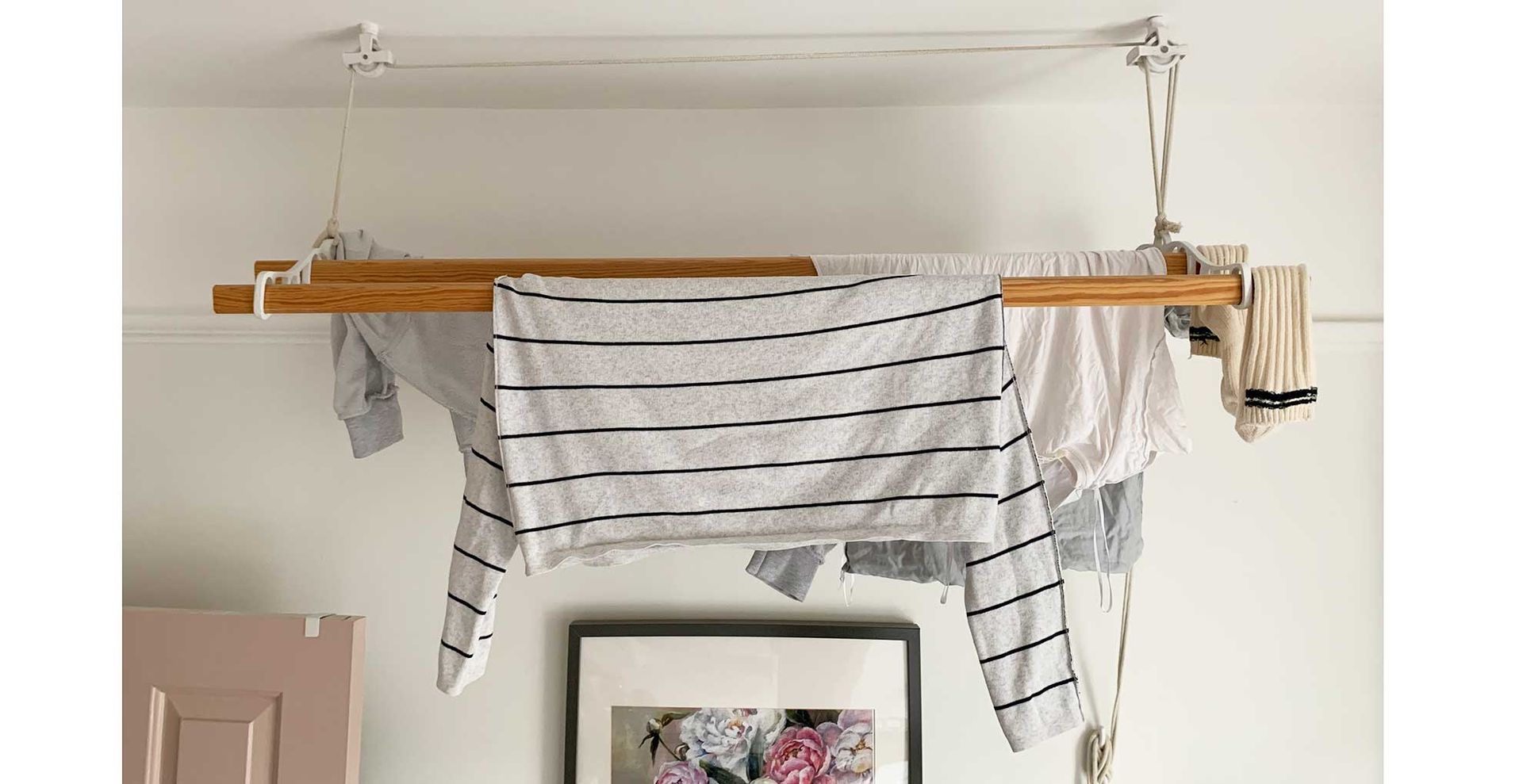 white kitchen with pink door and artwork with a drying rack suspended from the ceiling to suggest how to dry clothes indoors
