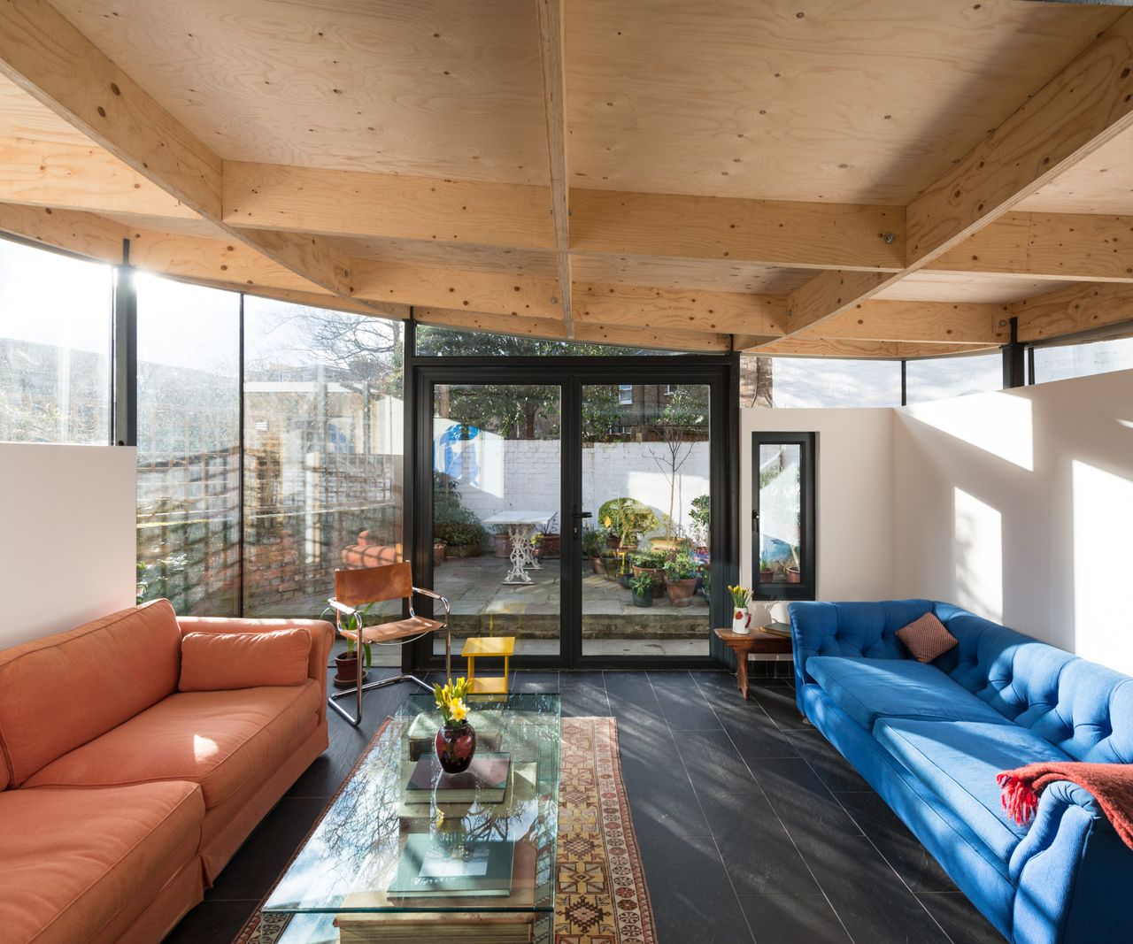 inside timber frame extension living room with wooden ceiling, blue and orange sofas and grey tiled floor