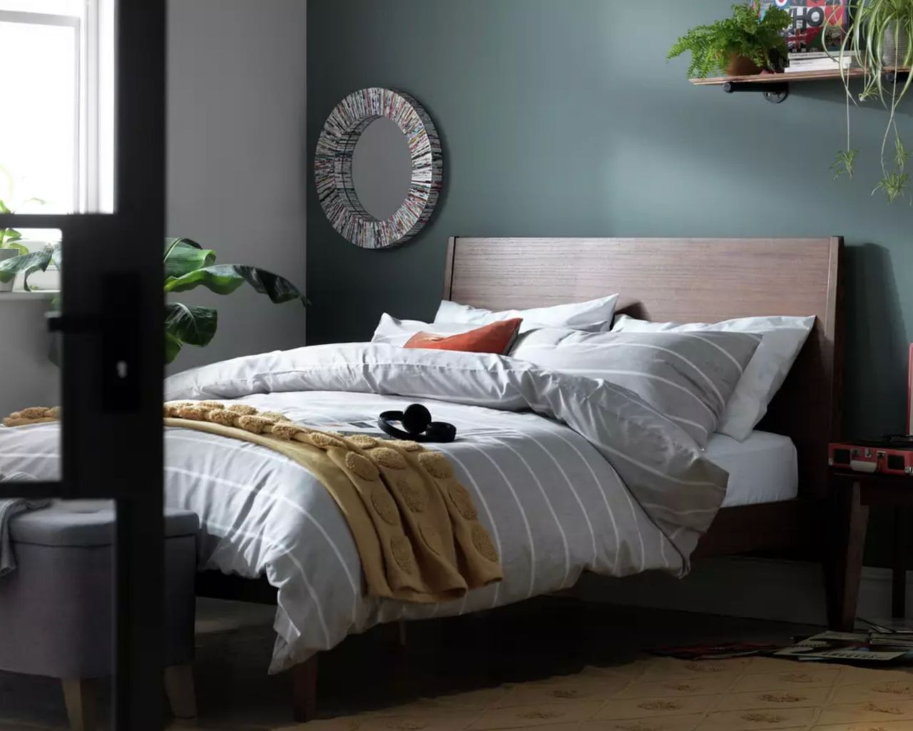 Dark wood bed frame in green bedroom with grey bedding and plants