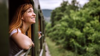 Woman looking out of train window into forest, smiling