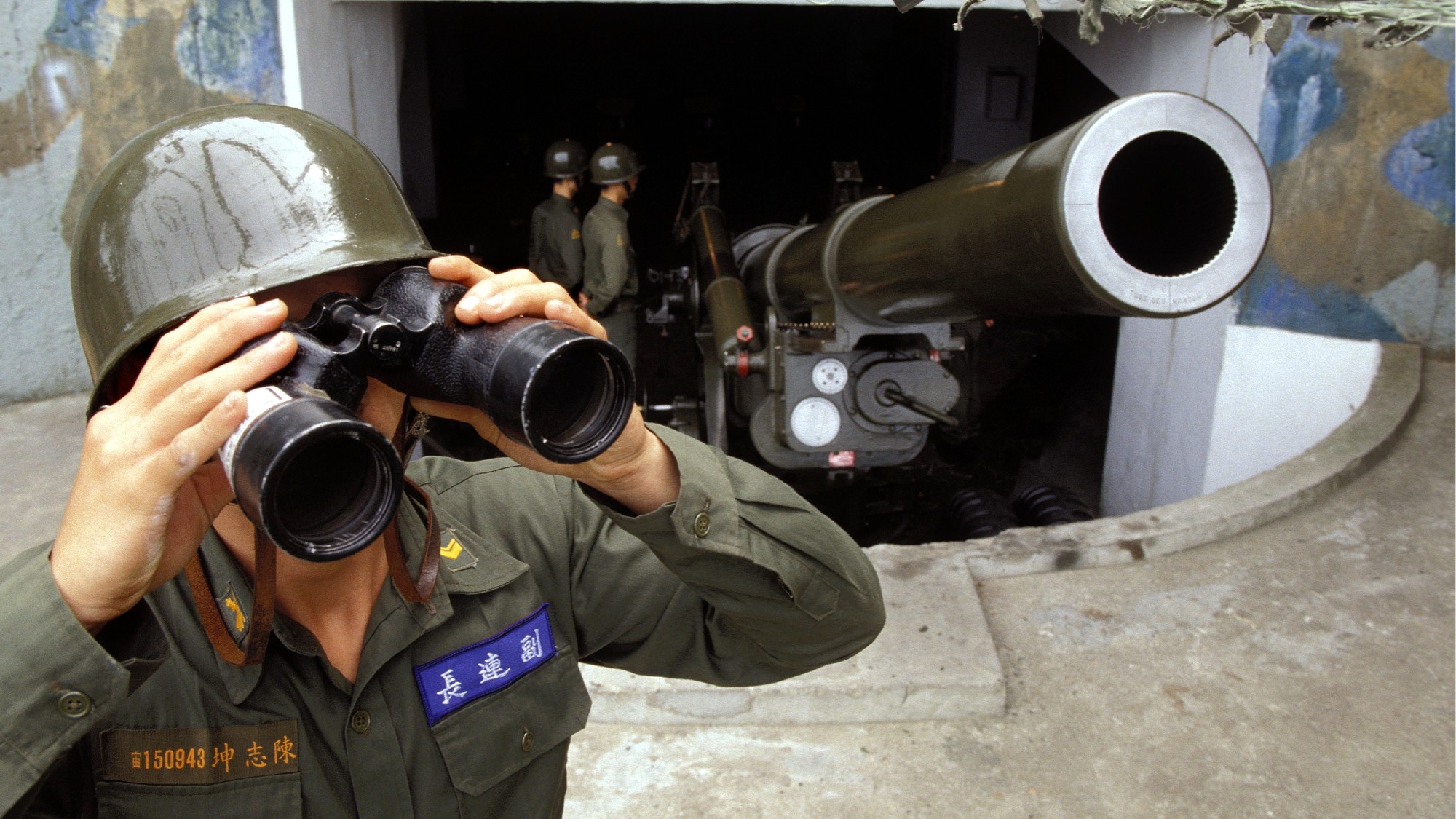 Taiwanese soldier looks through binoculars in front of an artillery gun