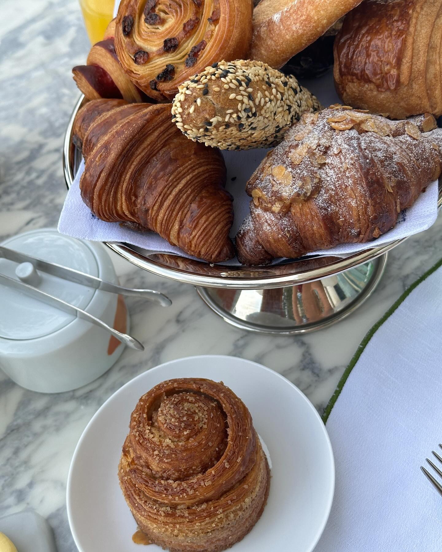 A photo of a selection of baked pastries, including cinnamon buns and almond croissants on a silver platter
