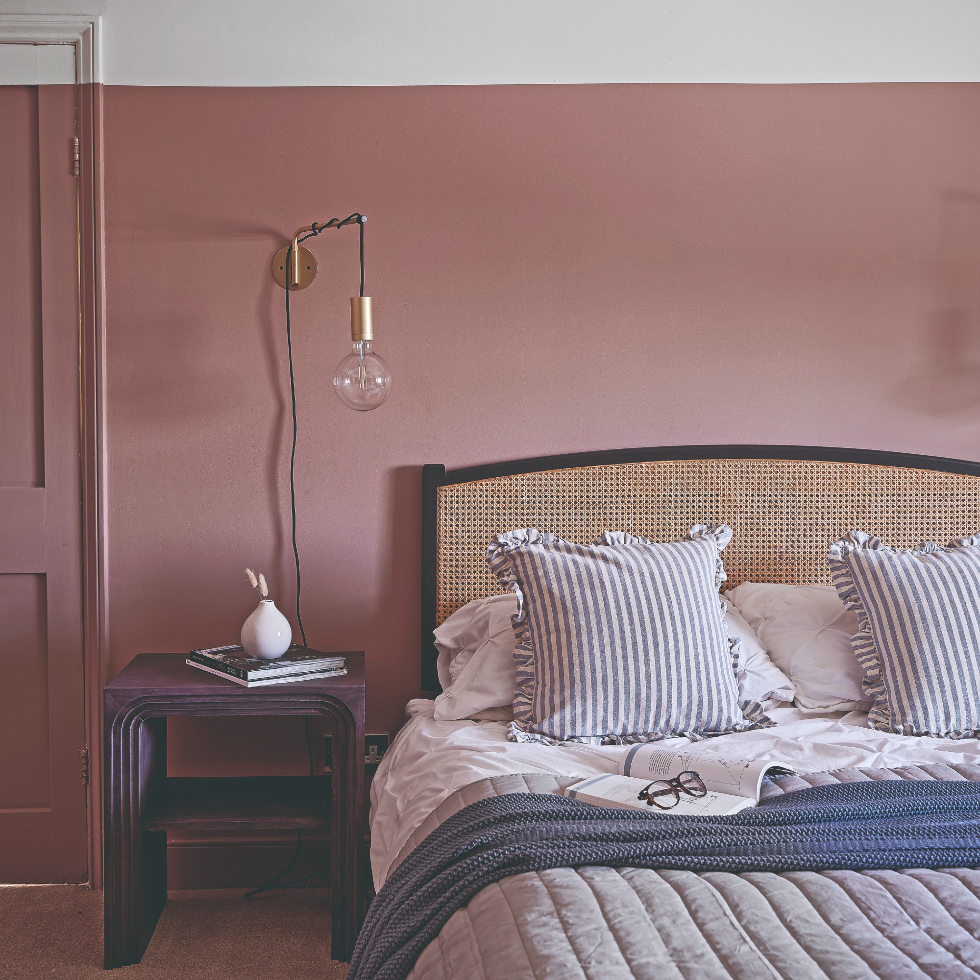 A living room painted in a vintage shade of pink with a rattan headboard